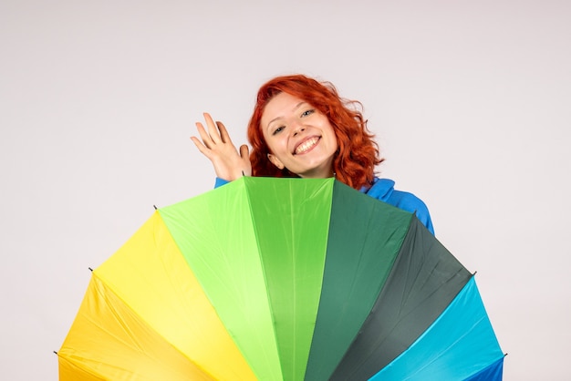 Front view of young female with colorful umbrella on white wall