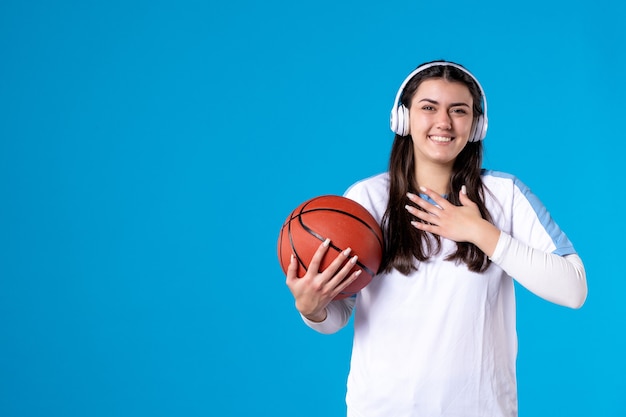 Free Photo front view young female with earphones holding basketball on blue wall