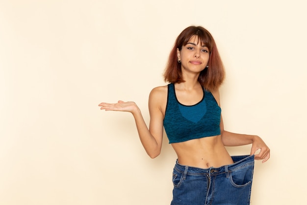 Front view of young female with fit body in blue shirt smiling on the light-white wall