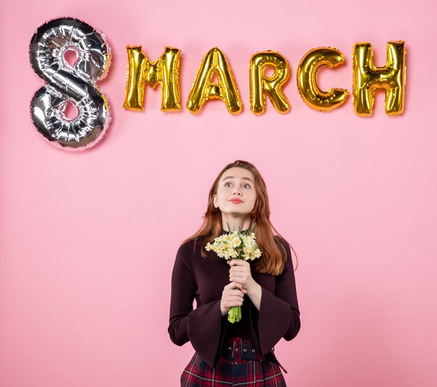 Front view young female with flowers in her hands and march decoration on pink background present womens day march marriage passion party equality