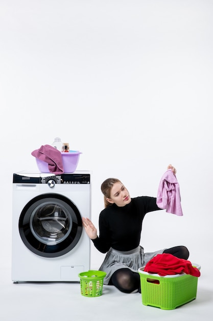 Front view young female with washing machine and dirty clothes onthe white wall