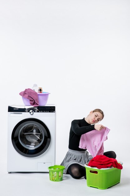 Front view of young female with washing machine and dirty clothes on white wall