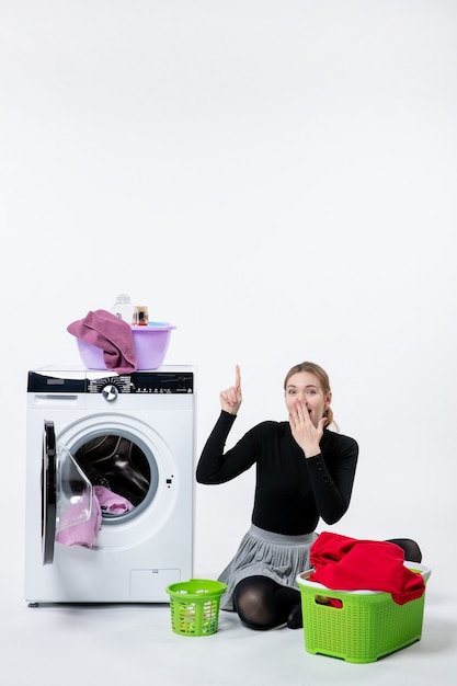 Front view of young female with washing machine folding dirty clothes on white wall