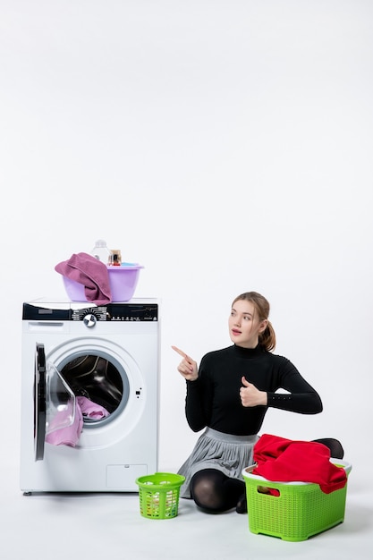 Front view of young female with washing machine folding dirty clothes on white wall