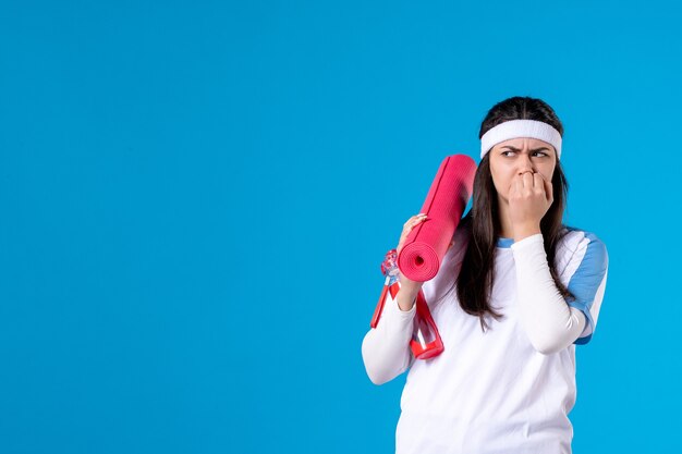 Front view young female with yoga mat on blue wall