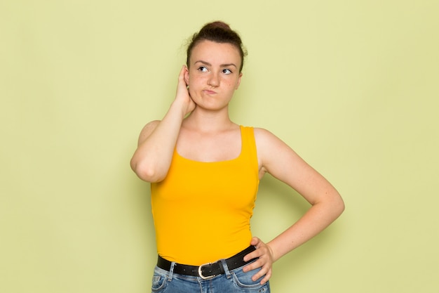 A front view young female in yellow shirt and blue jeans with thinking expression