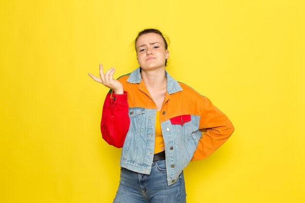 A front view young female in yellow shirt colorful jacket and blue jeans posing