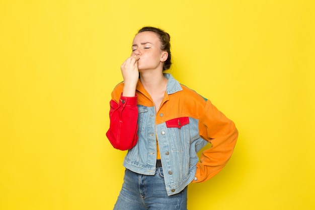 A front view young female in yellow shirt colorful jacket and blue jeans showing tasty sign