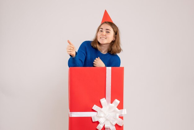 Front view of young girl inside red present box on white wall