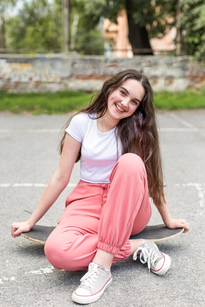 Front view young girl posing while sitting on her skateboard