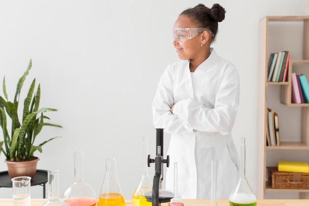 Free photo front view of young girl scientist in lab coat with microscope and copy space