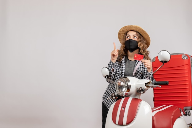 Free Photo front view young girl with black mask holding ticket pointing up, standing near red moped