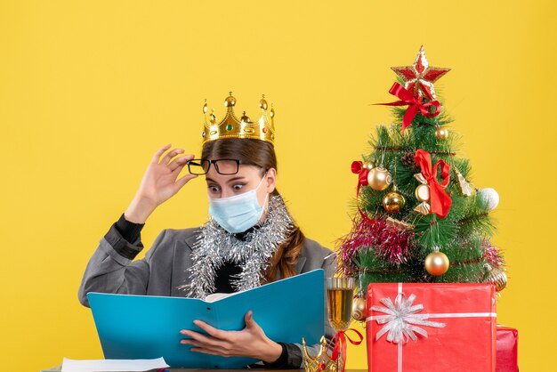 Front view young girl with crown putting off her eyeglasses xmas tree and gifts cocktail