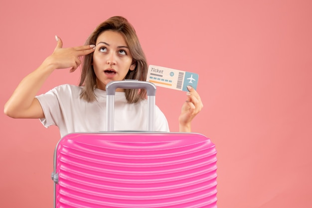 Free photo front view young girl with pink suitcase holding ticket putting finger gun on her temple