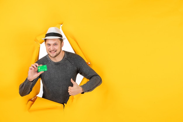 Free photo front view of young guy holding bank card and making ok gesture in a torn on yellow wall