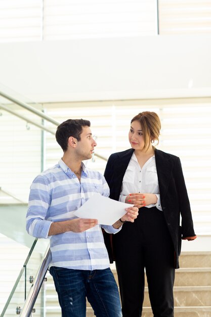 A front view young handsome man in striped shirt talking and discussing work issues with young businesswoman during daytime work activity building