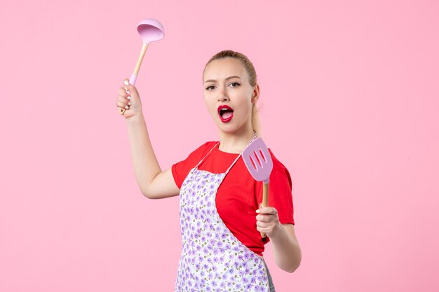 Front view young housewife holding cutlery on pink wall