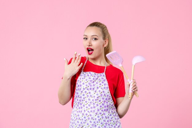 Front view young housewife posing with cutlery in her hands on pink wall