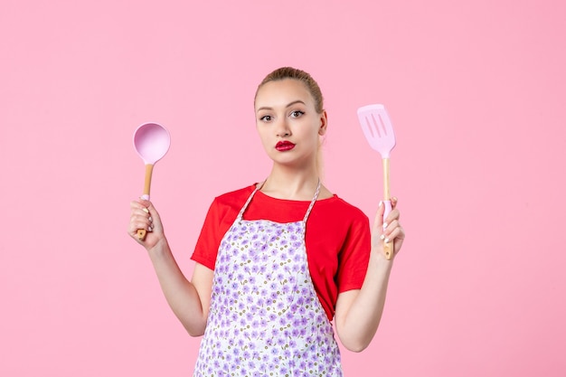 Front view young housewife posing with cutlery on pink wall