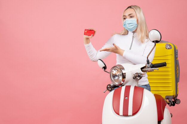 Front view young lady on moped with yellow suitcase holding credit card