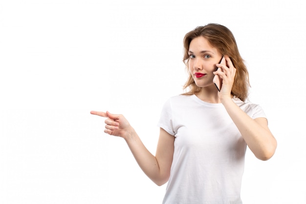 A front view young lady in white shirt and black modern jeans posing talking on the phone on the white