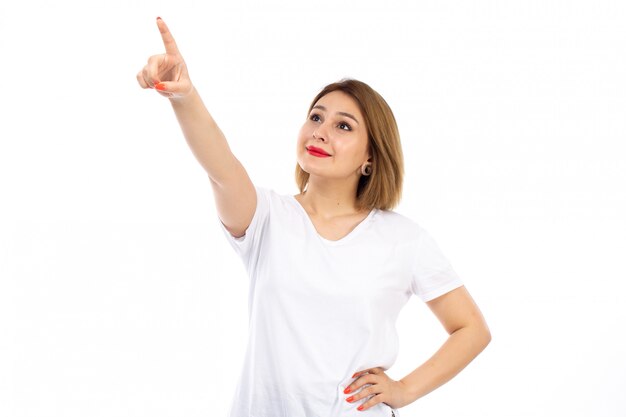 A front view young lady in white t-shirt posing pointing into the skies smiling on the white