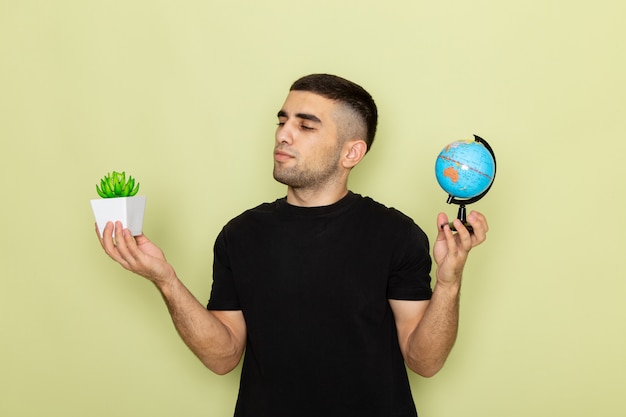 Front view young male in black t-shirt holding little green plant and little globe on green