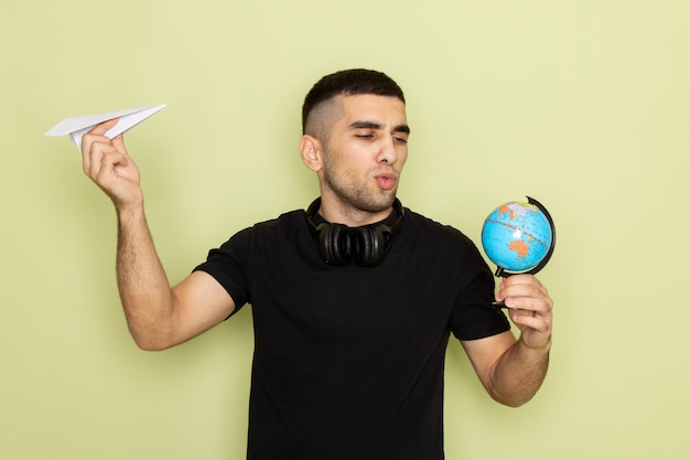 Free photo front view young male in black t-shirt holding paper plane and little globe on green