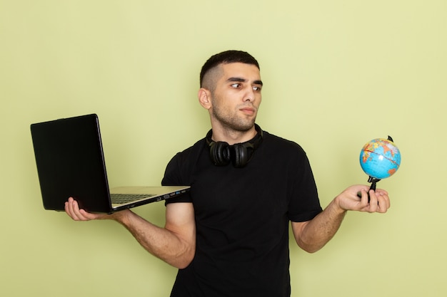 Free Photo front view young male in black t-shirt using laptop holding little globe on green