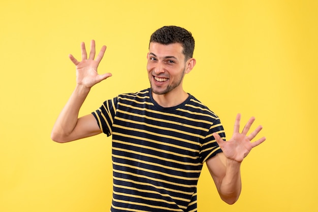 Front view young male in black and white striped t-shirt opening hands on yellow isolated background