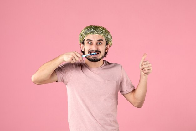 front view young male cleaning his teeth on pink background