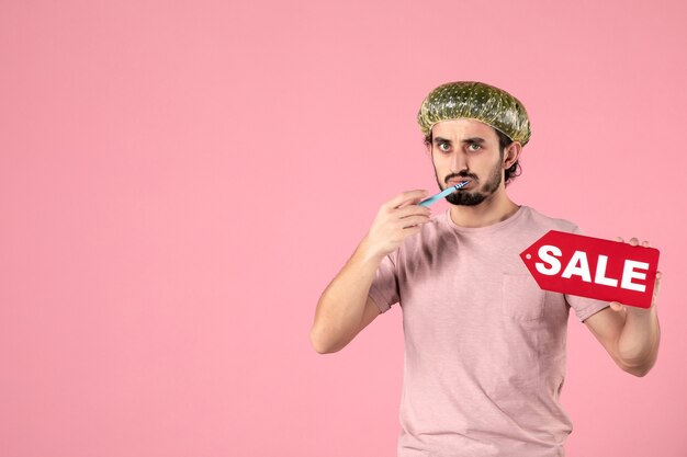 front view young male cleaning his teeth and sale nameplate on pink background