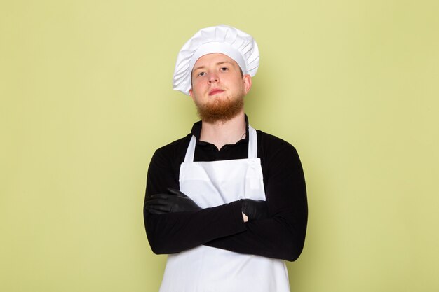 A front view young male cook in black shirt with white cape white head cap in black gloves posing