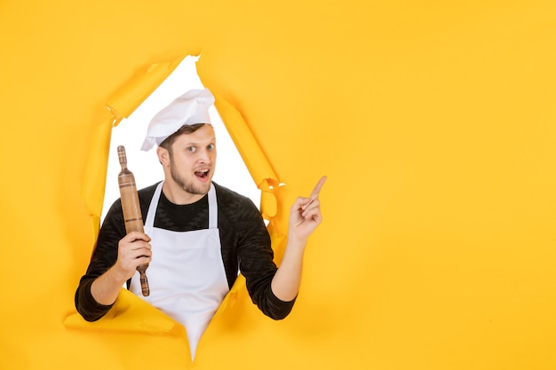 Front view young male cook in white cape holding rolling pin on the yellow background food white man photo color kitchen job