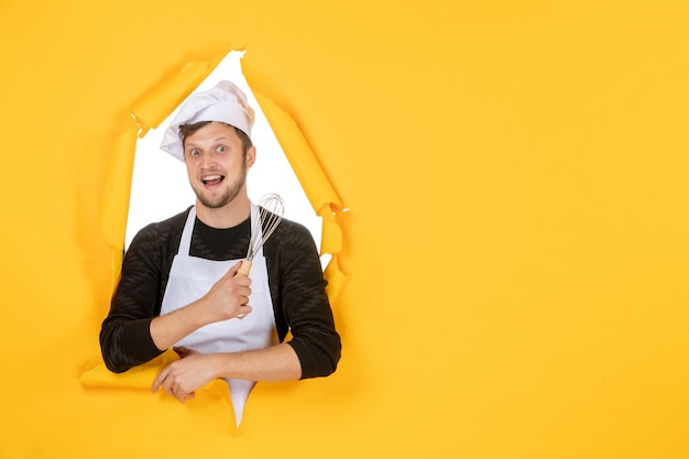 Front view young male cook in white cape holding whisk on the yellow background photo food man cuisine kitchen job color white