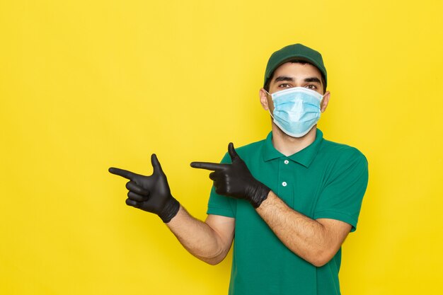 Front view young male courier in green shirt green cap black gloves posing on yellow