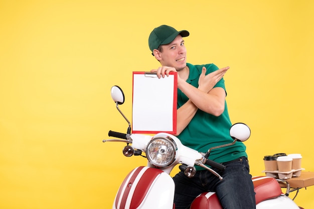 Front view young male courier in green uniform holding file note on yellow 