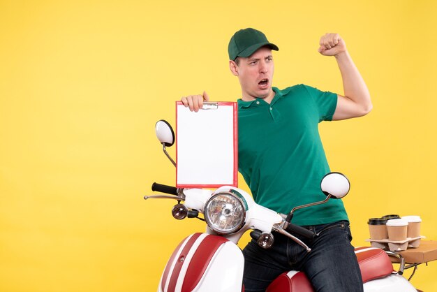 Front view young male courier in green uniform holding file note on yellow 