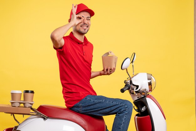 Front view young male courier in red uniform with delivery food on yellow background