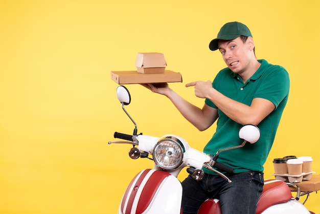 Front view young male courier in uniform holding food packages on a yellow 