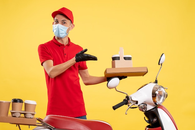 Front view young male courier in uniform with coffee and food box on yellow background