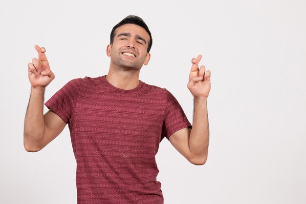 Front view young male in dark-red t-shirt crossing his fingers on white background