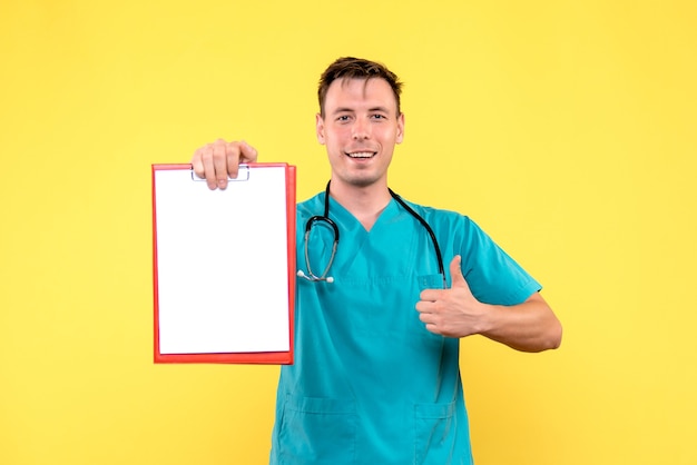 Front view of of young male doctor holding analyzes on yellow wall