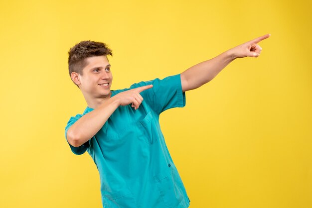 Front view young male doctor in medical suit on yellow background