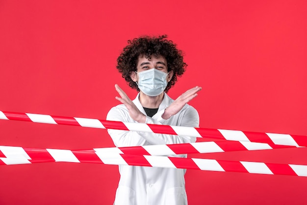 Free photo front view young male doctor in medical uniform and mask on red background isolation drug covid danger warning health quarantine