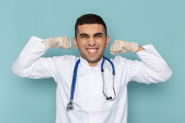 Front view of young male doctor in white suit with blue stethoscope flexing