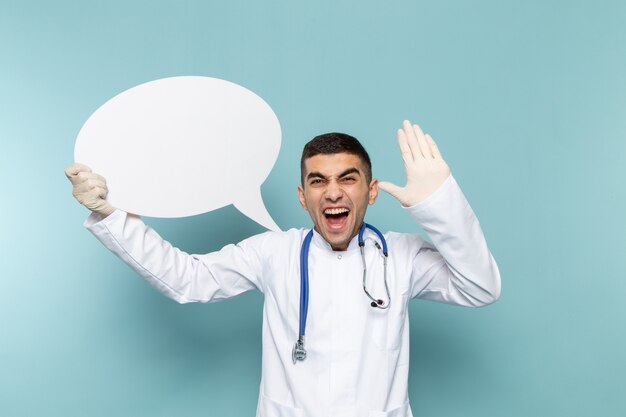 Front view of young male doctor in white suit with blue stethoscope holding white sign