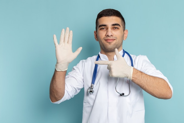 Free photo front view of young male doctor in white suit with blue stethoscope pointing to the glove