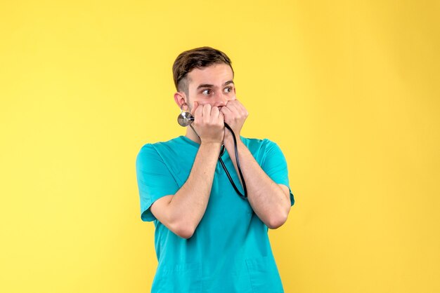 Front view of young male doctor with stethoscope on yellow wall