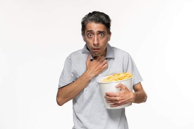 Front view young male eating potato chips and watching movie on a light-white surface